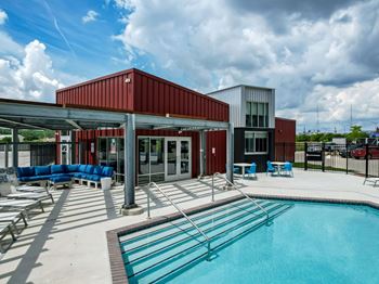 A swimming pool area with a red building and blue seating.